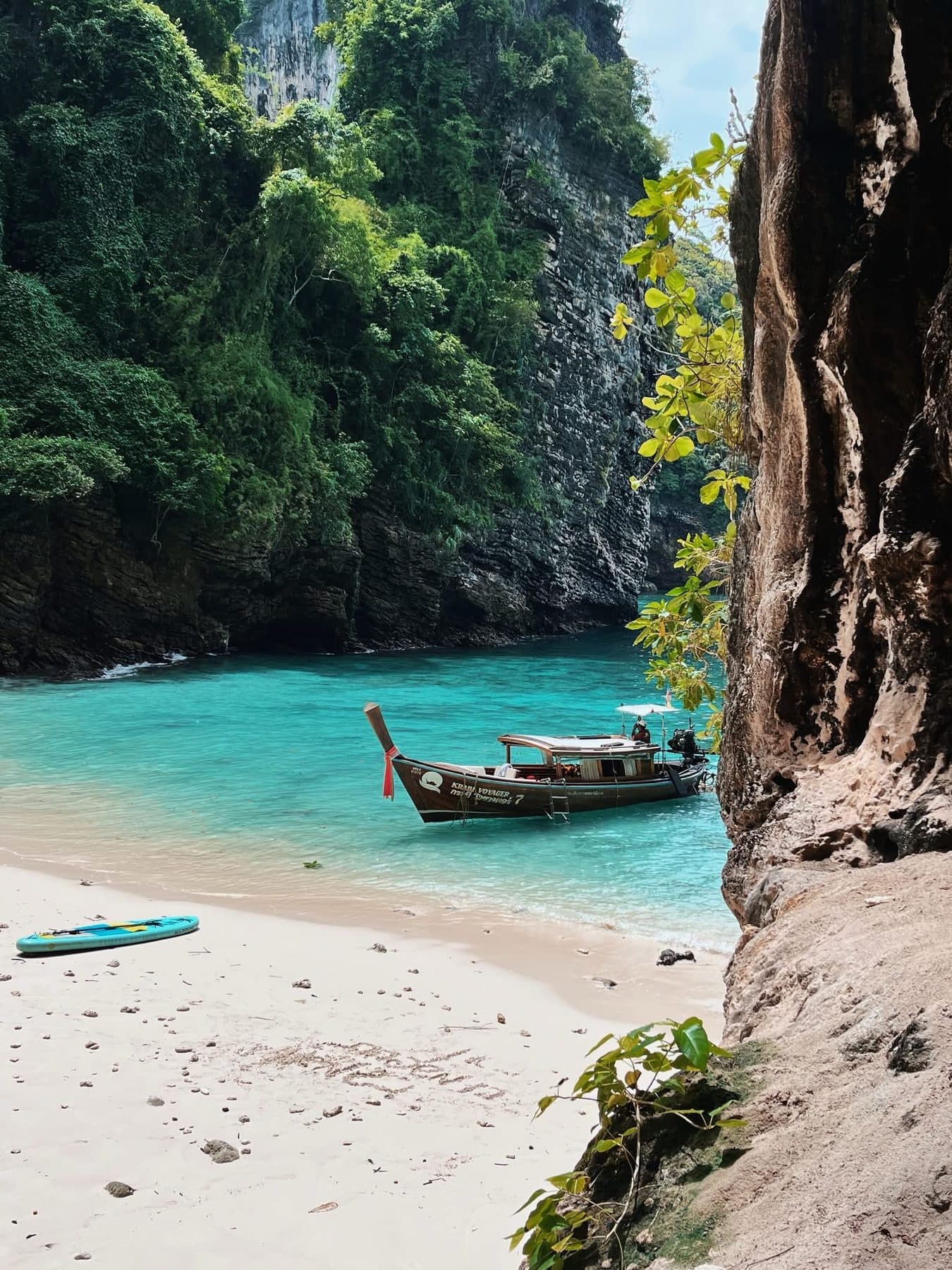 Krabi Voyager 长尾船停泊在隐秘的海湾中,沙滩上放着一块桨板