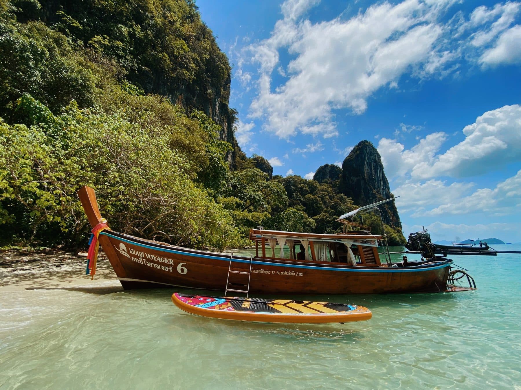 Krabi Voyager 6 号停在一座石灰岩岛屿旁,清澈的海水中漂着一块桨板